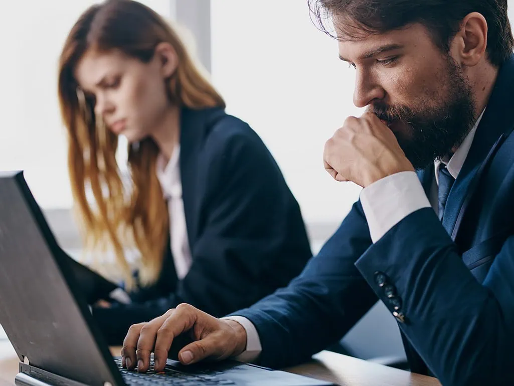 Business professionals in suits looking concerned while working on laptops during a manual supplier registration process for every project